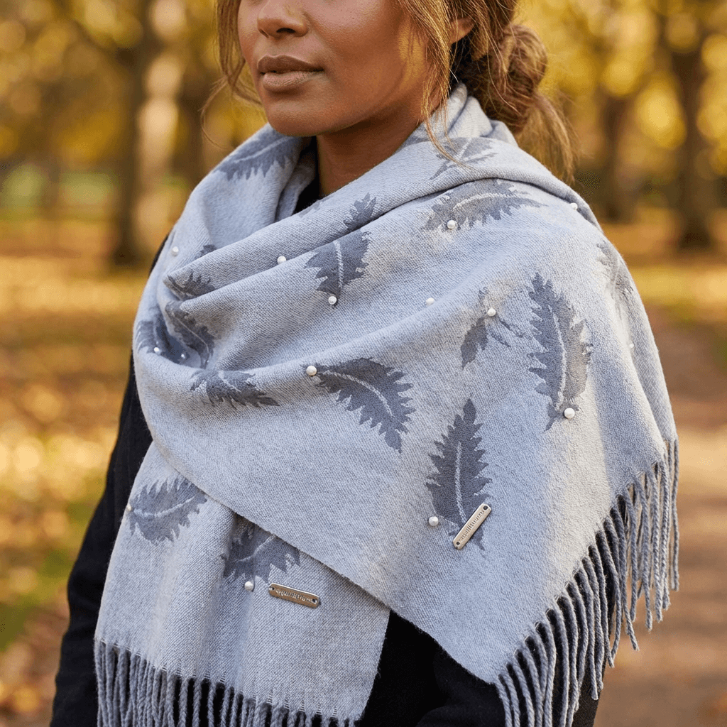 Woman wearing a gray patterned scarf with fringes in an outdoor setting