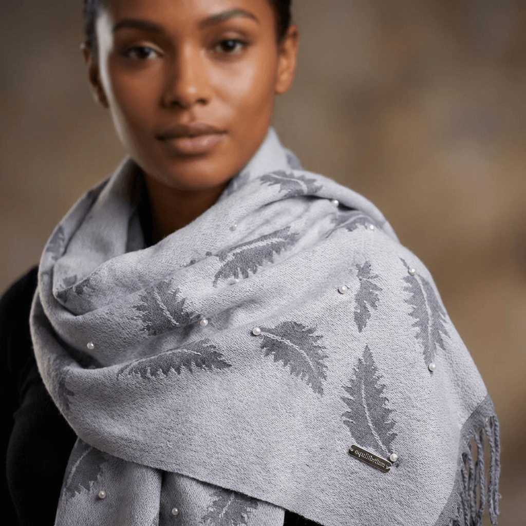 Woman wearing a gray scarf with leaf patterns and pearl embellishments on a blurred background