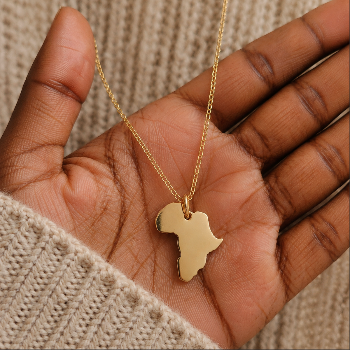 Gold necklace with an Africa-shaped pendant held in a hand against a textured background