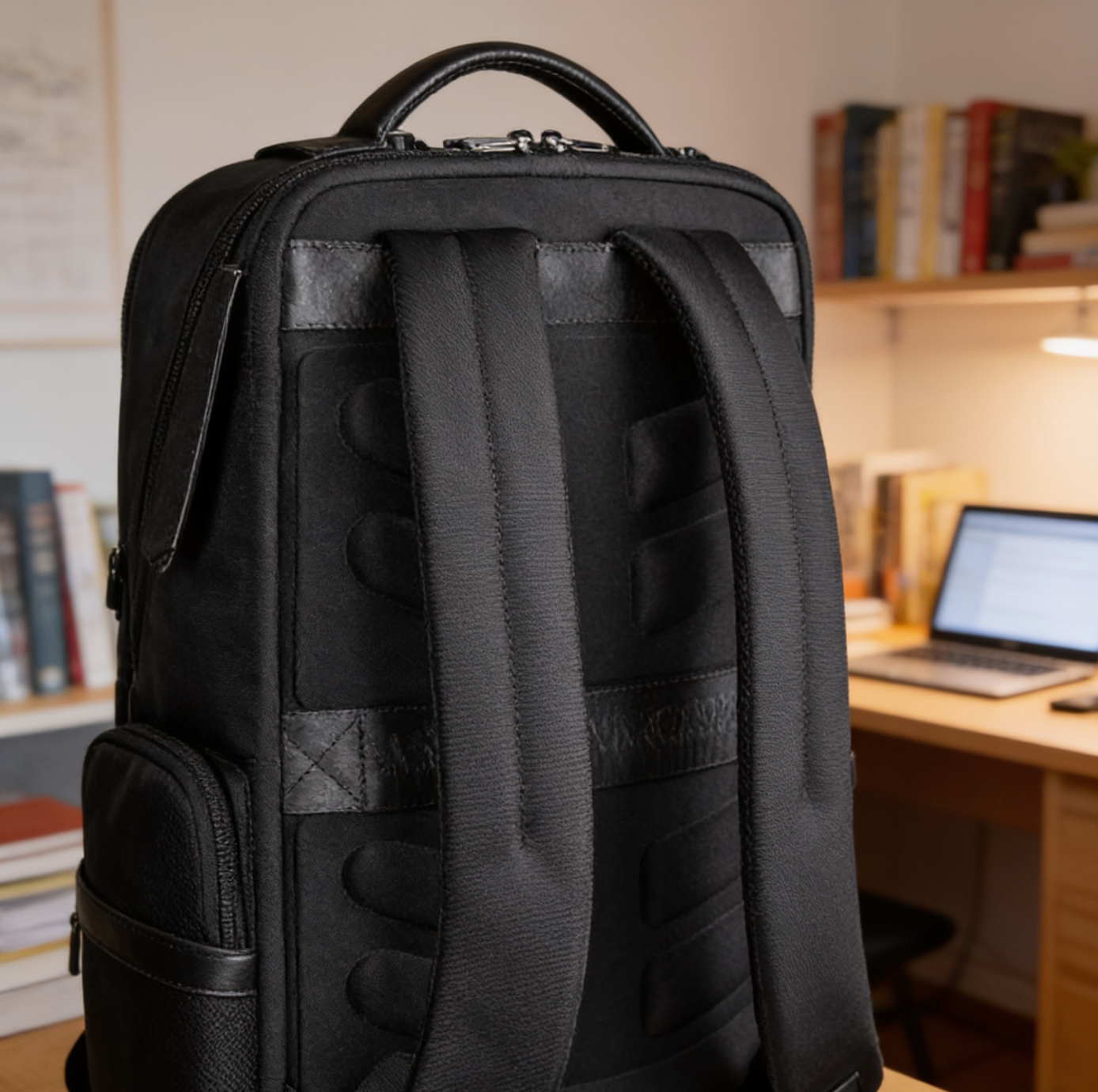Black backpack with a desk and laptop in the background
