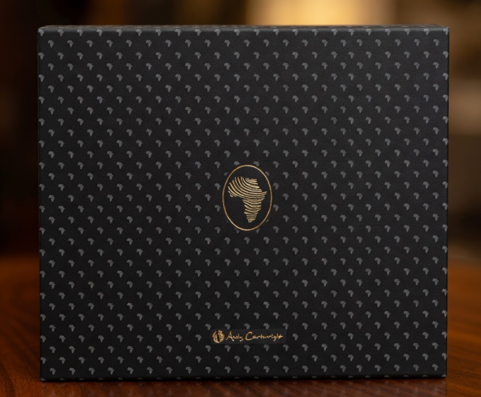 Black box with gold patterns and logo on a wooden surface