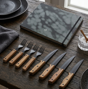 Set of knives and forks with wooden handles on a wooden table.