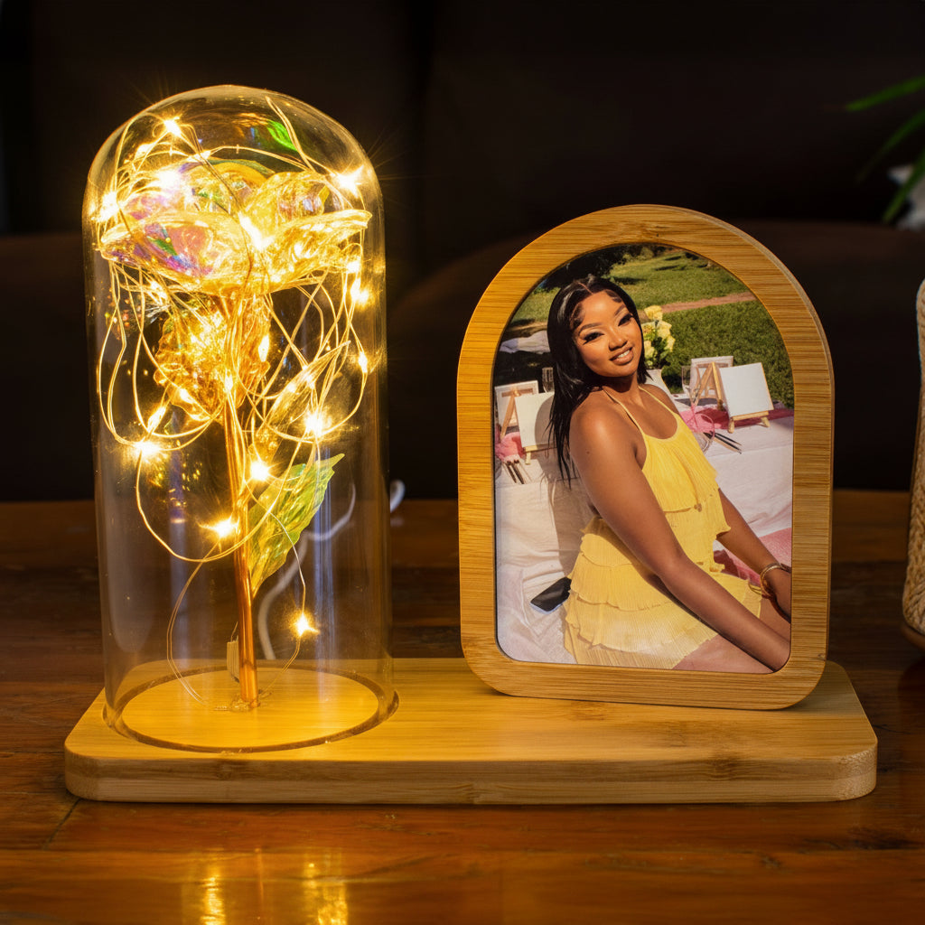 Decorative setup with a glass dome containing a colorful flower and a wooden photo frame with a woman's portrait.