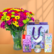 Bouquet of colorful flowers with a gift bag, tea box, and candle on an orange background