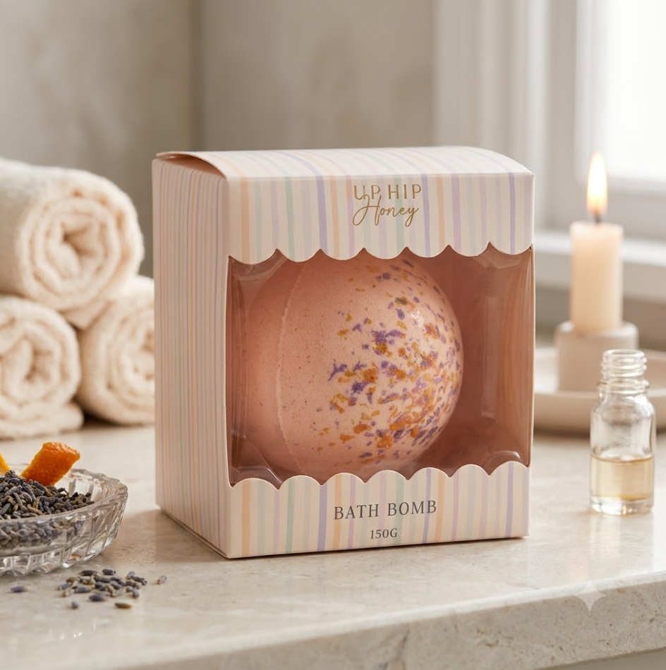 Bath bomb in a decorative box on a bathroom counter with towels and a candle in the background.