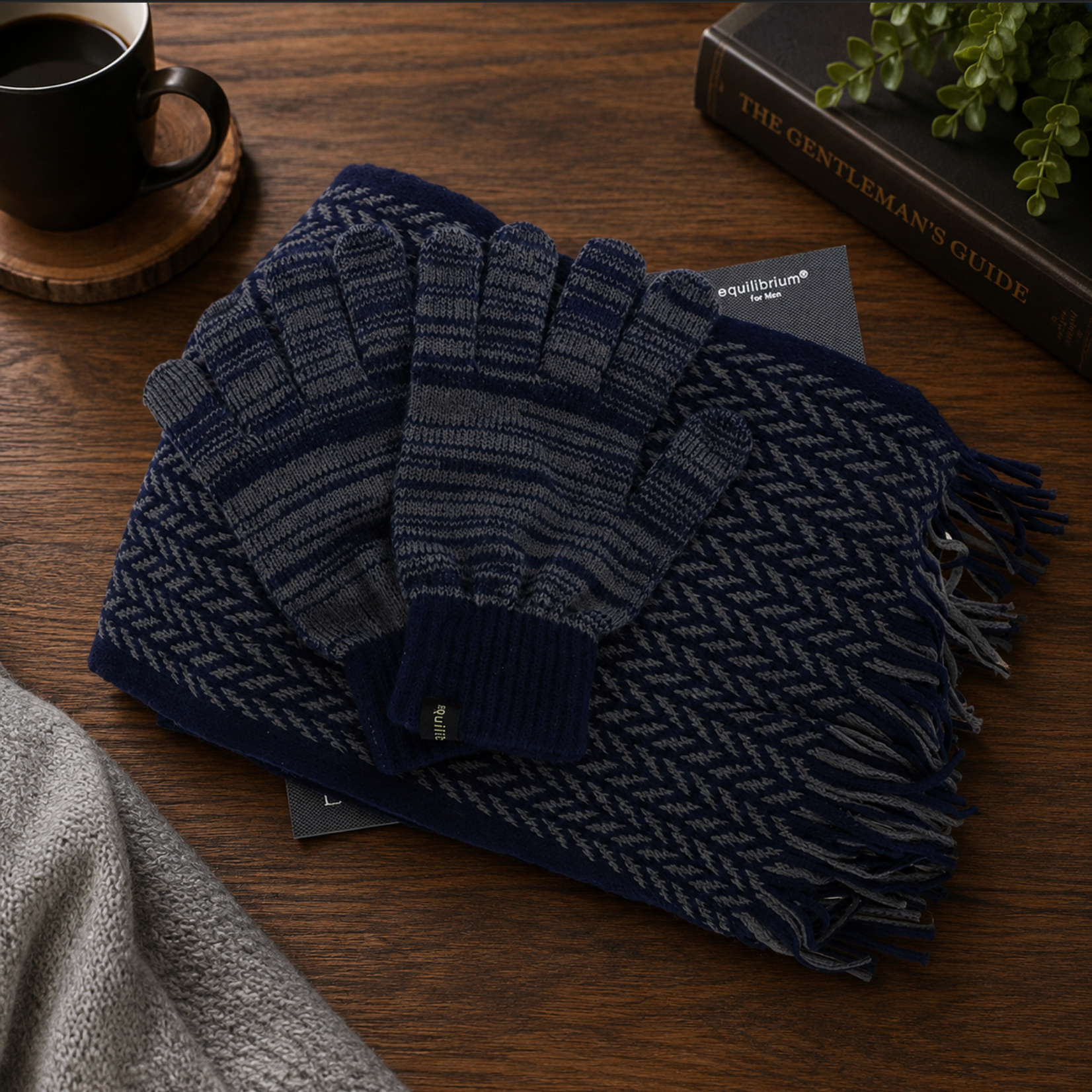 Navy herringbone scarf and gloves on a wooden surface with a book and cup in the background