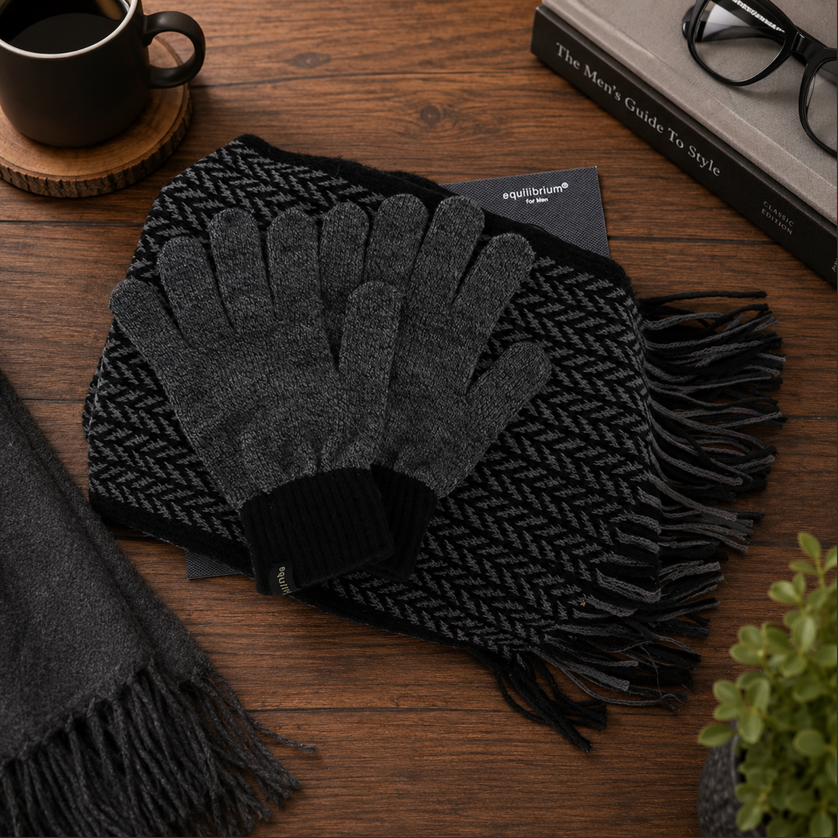 Dark gray gloves and scarf on a wooden surface with a book and coffee cup in the background.