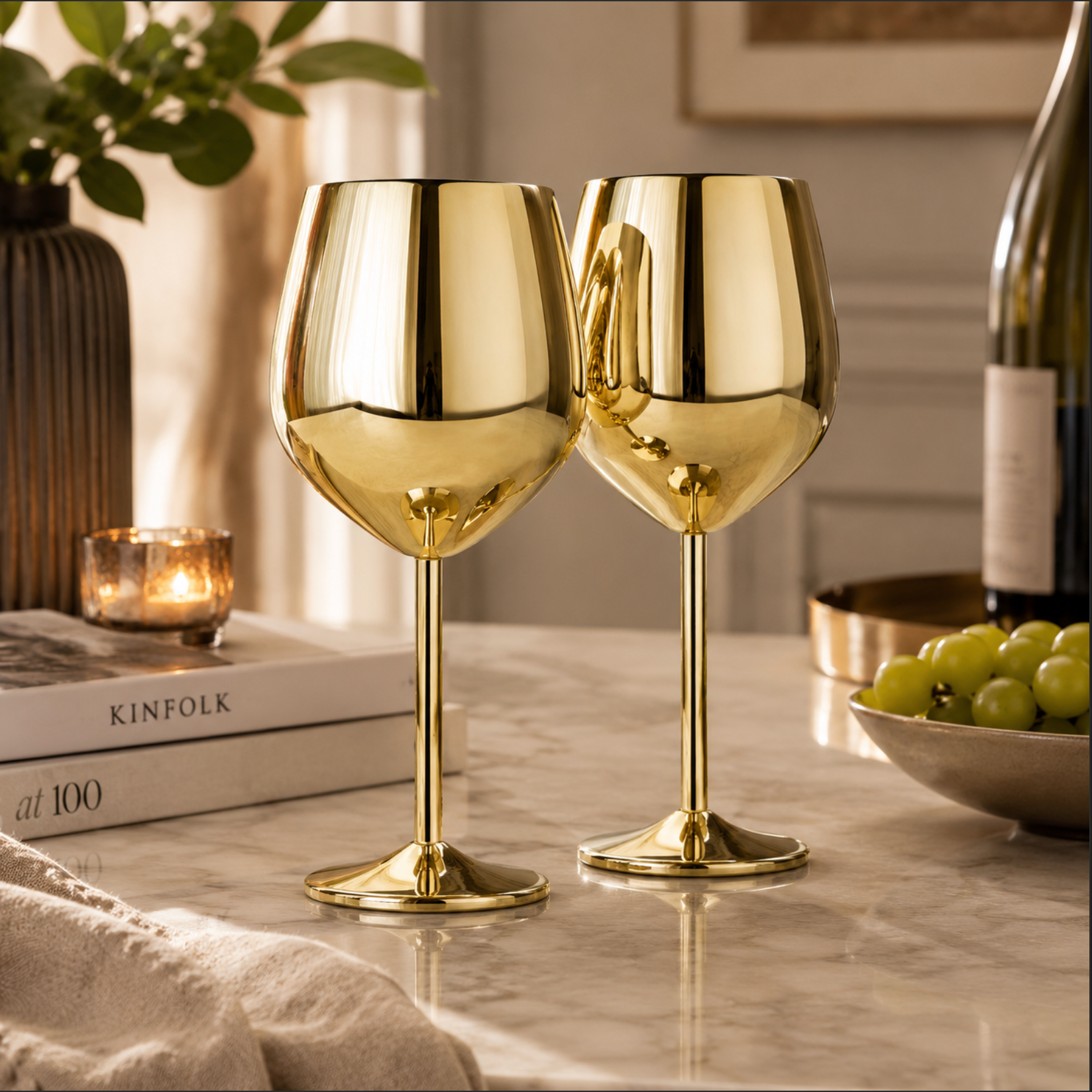 Two gold wine glasses on a table with a bottle of wine and grapes in the background.