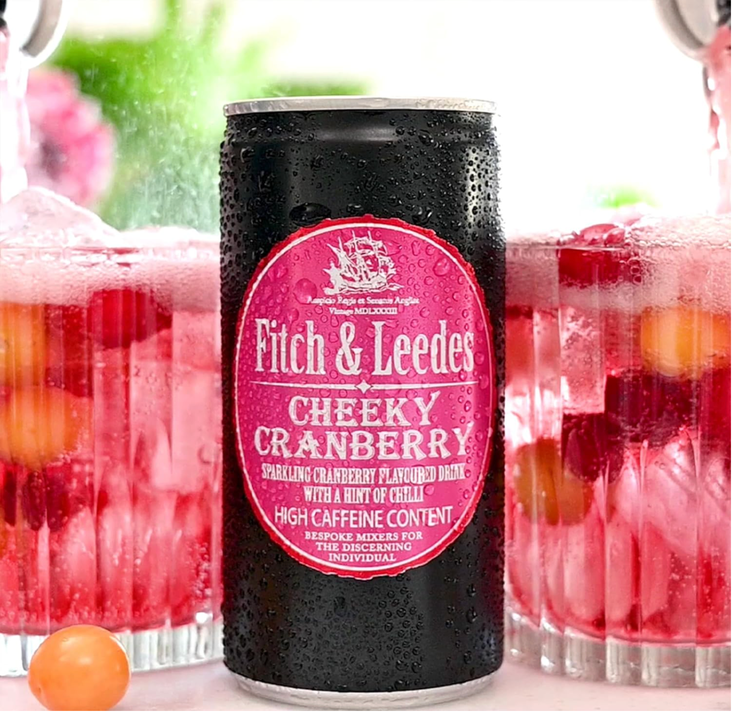 Fitch & Leedes Cheeky Cranberry can with glasses of cranberry juice in the background