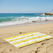 A yellow and white striped towel on a sandy beach with ocean and rocks in the background
