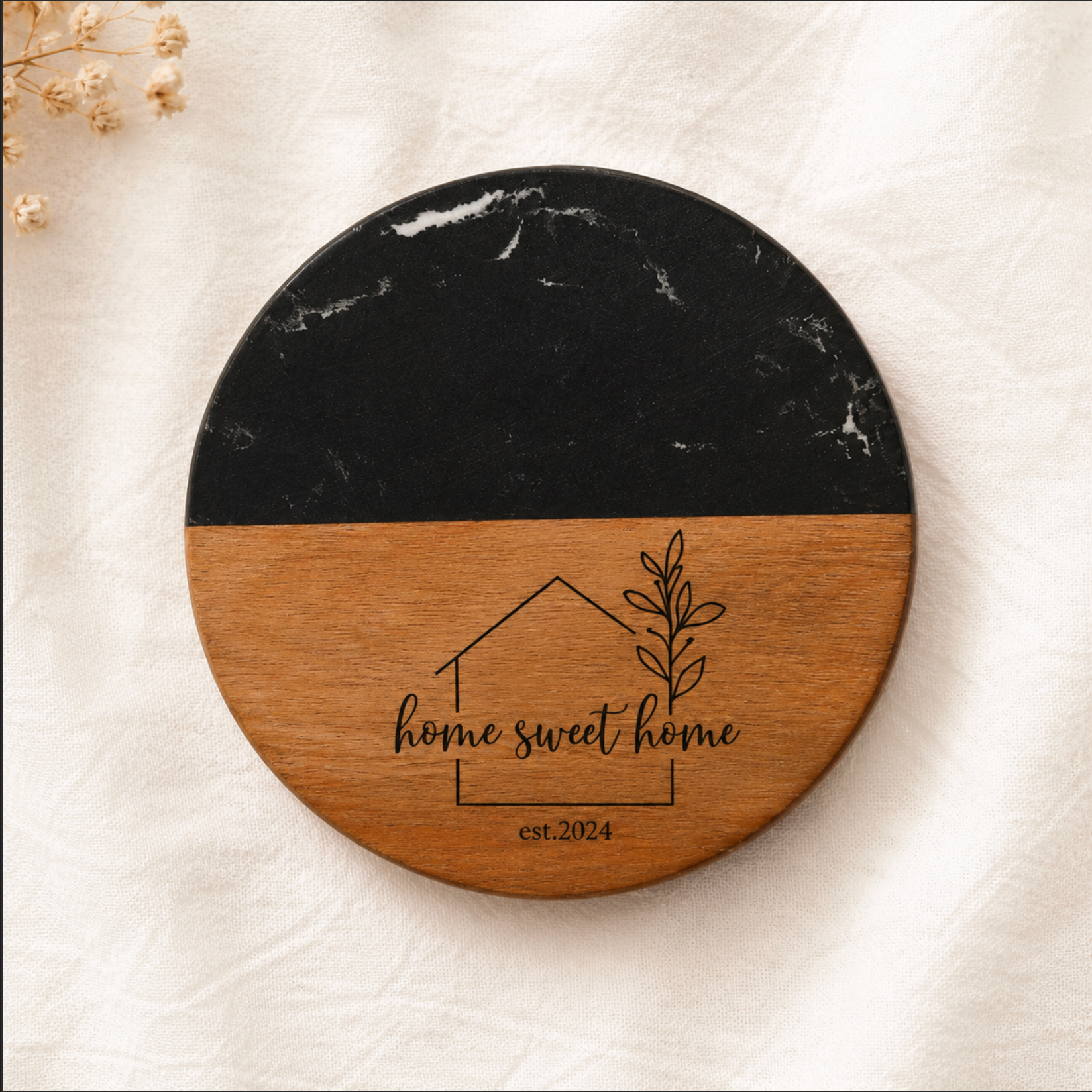 Round wooden and black marble coaster with 'home sweet home' engraving on a light background