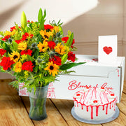 Bouquet of colorful flowers in a vase, a cake with red drizzle, and a card on a wooden surface.