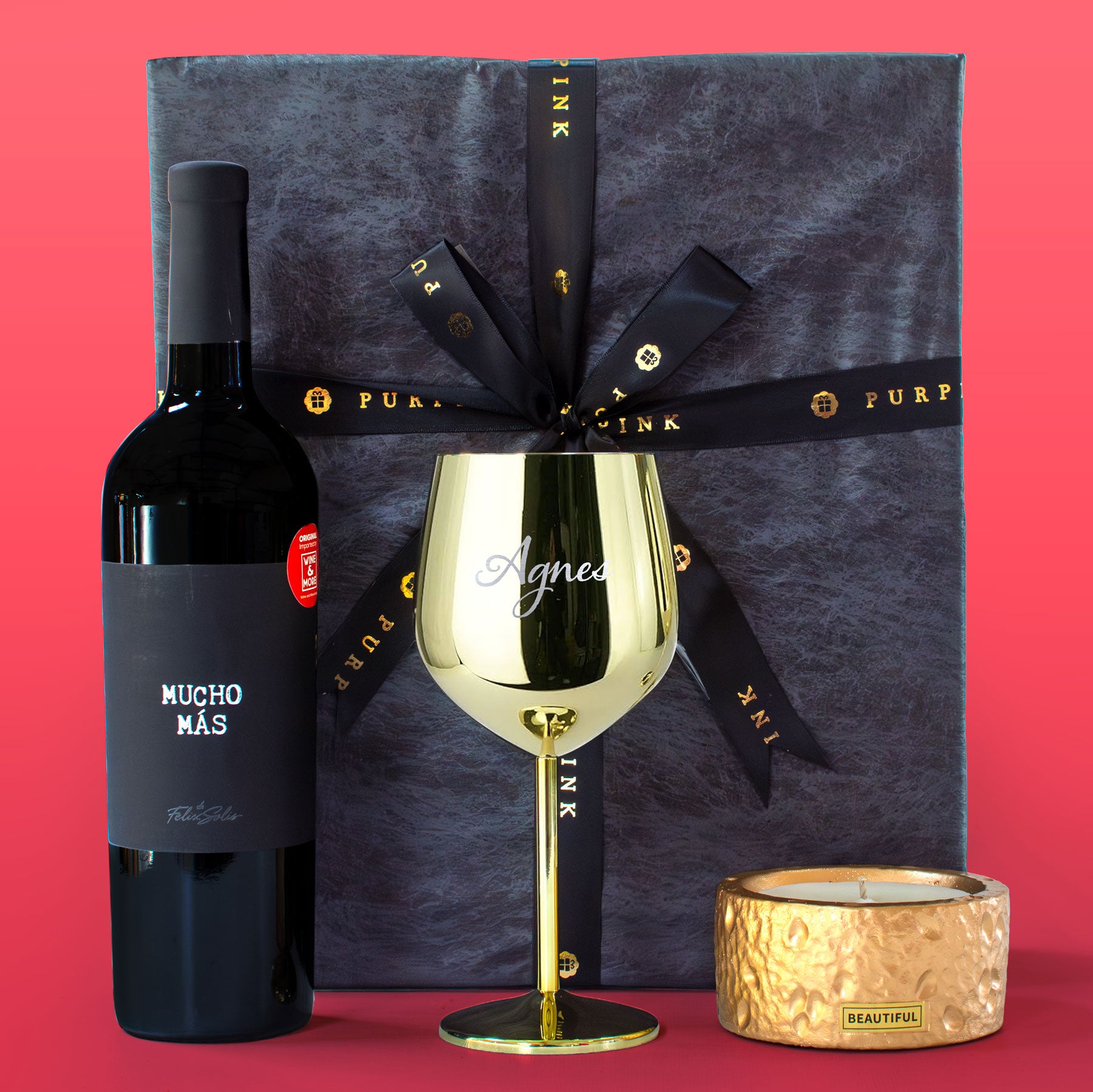 Wine bottle, gold wine glass, and candle with a branded gift box on a red background