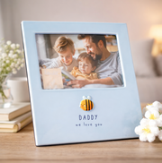 Light blue photo frame with a picture of a father and two children, placed on a wooden surface with flowers and books in the background.