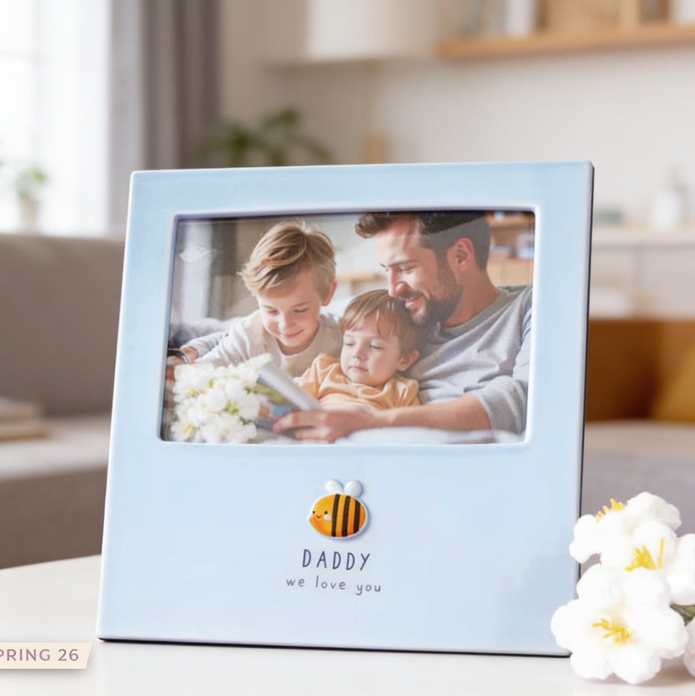 Light blue photo frame with a family picture and 'Daddy we love you' text, placed on a surface with flowers.
