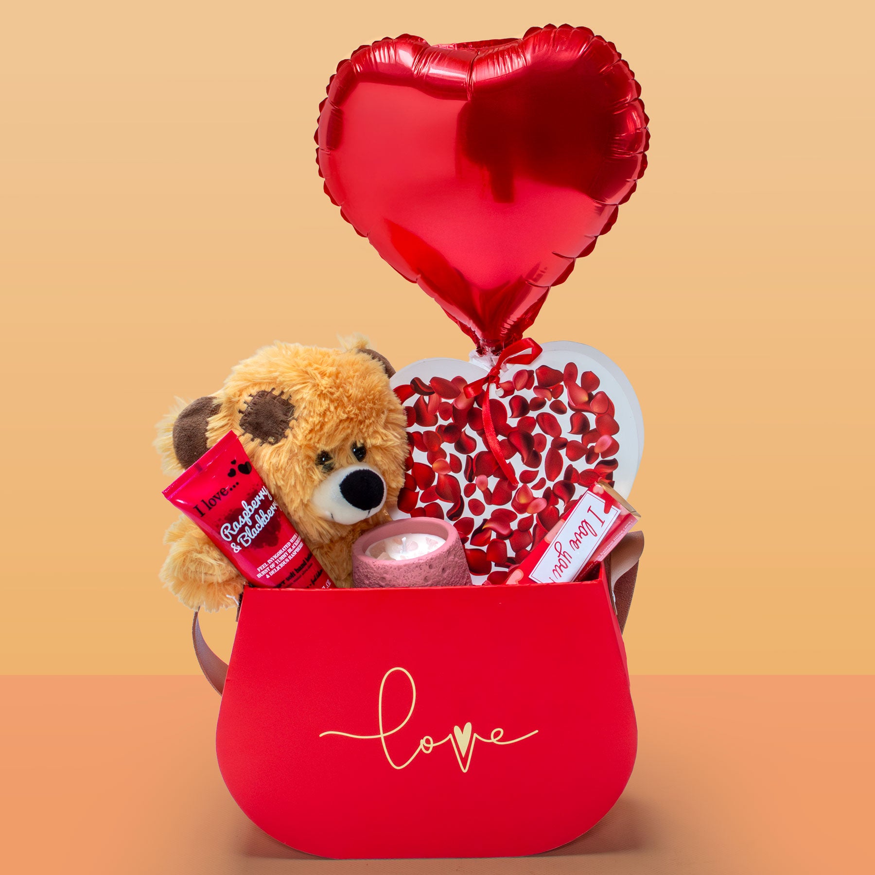 Red gift box with teddy bear, heart-shaped balloon, and candy on a beige background