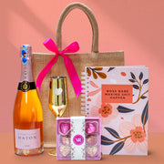 Gift set with champagne, chocolates, and a notebook on a pink background