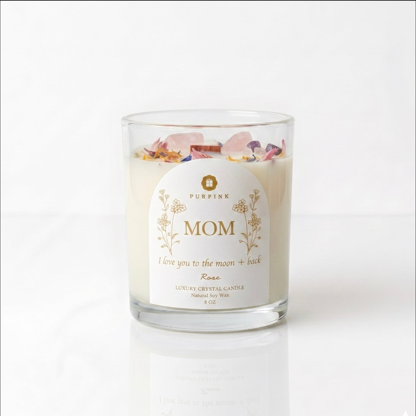 A luxury crystal candle in a clear glass jar with a white label reading 'MOM' and 'Purpink' at the top, decorated with dried rose petals on a white background.