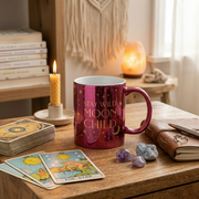 Mug with 'Stay Wild Moon Child' text on a table with tarot cards, candles, and crystals.