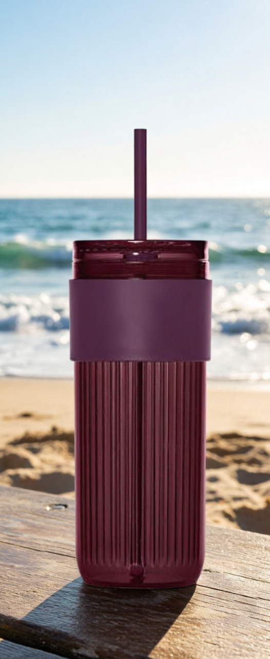 Maroon tumbler with a straw on a wooden surface by the beach