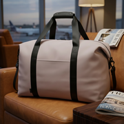 White duffel bag with black straps on a brown leather couch in an airport lounge.