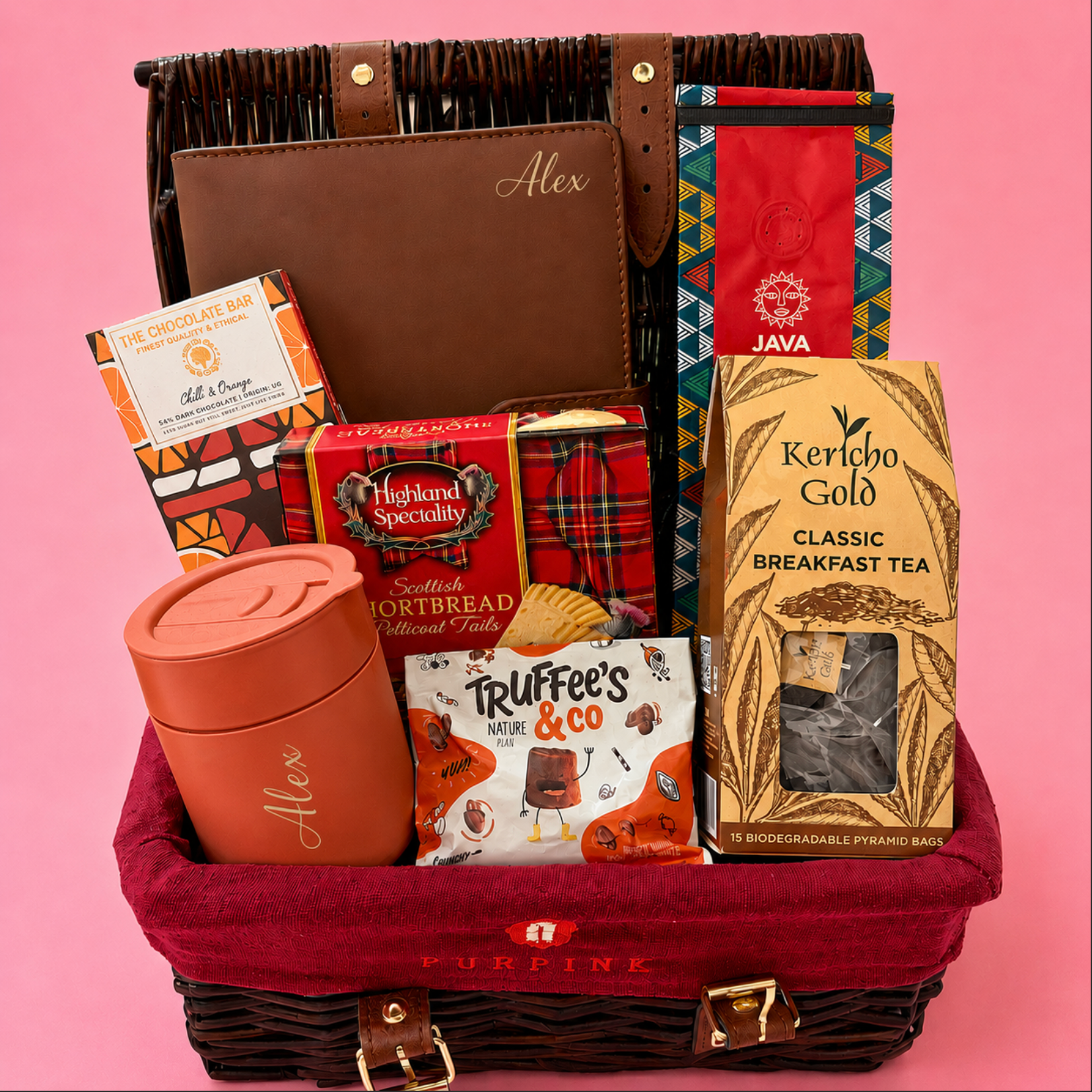 Gift basket with tea, snacks, and a mug on a pink background