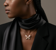 Woman wearing a black scarf and gold necklace with a butterfly pendant against a neutral background