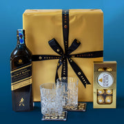 Johnnie Walker Double Black bottle with a gold gift box, glasses, and chocolate truffles on a blue background