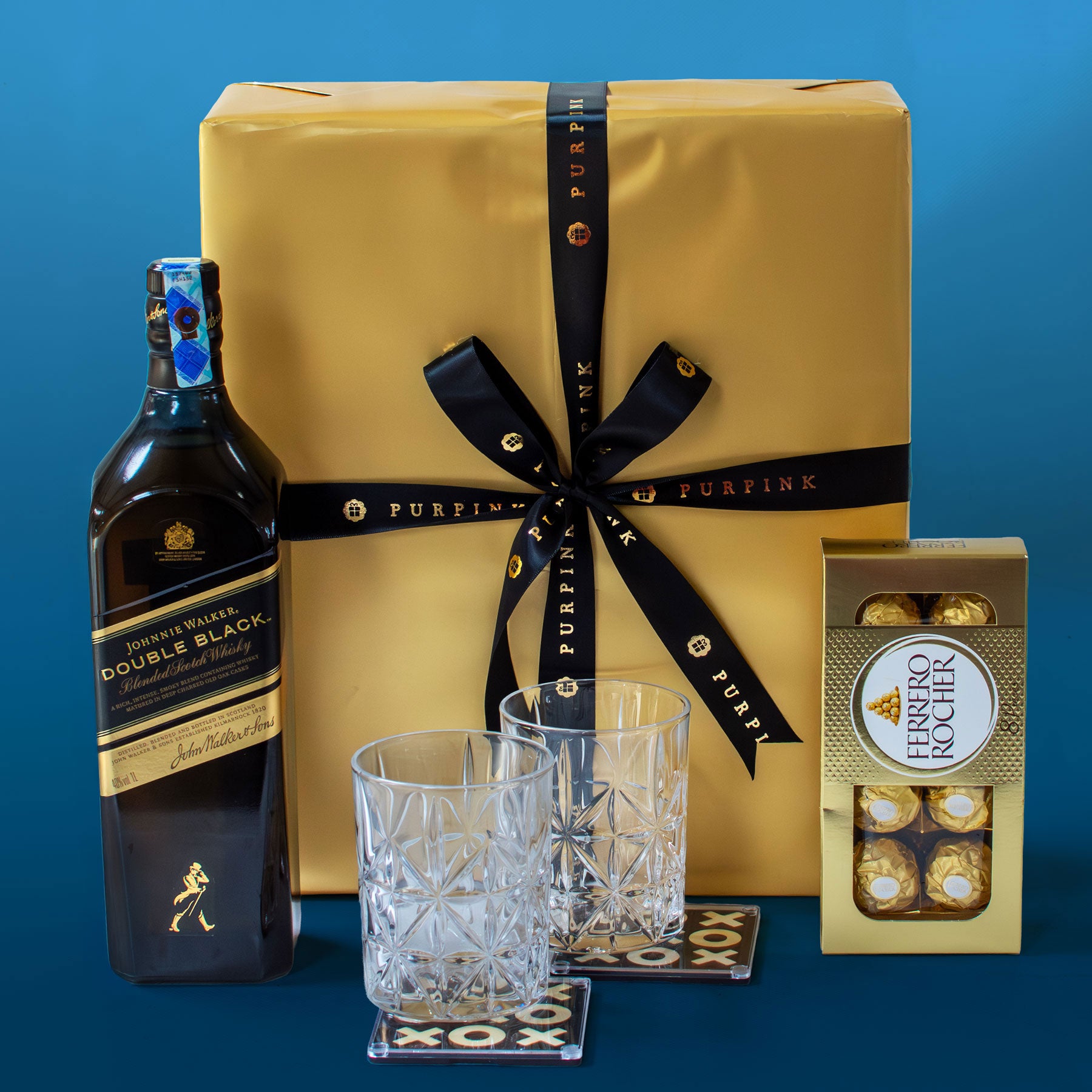 Johnnie Walker Double Black bottle with a gold gift box, glasses, and chocolate truffles on a blue background