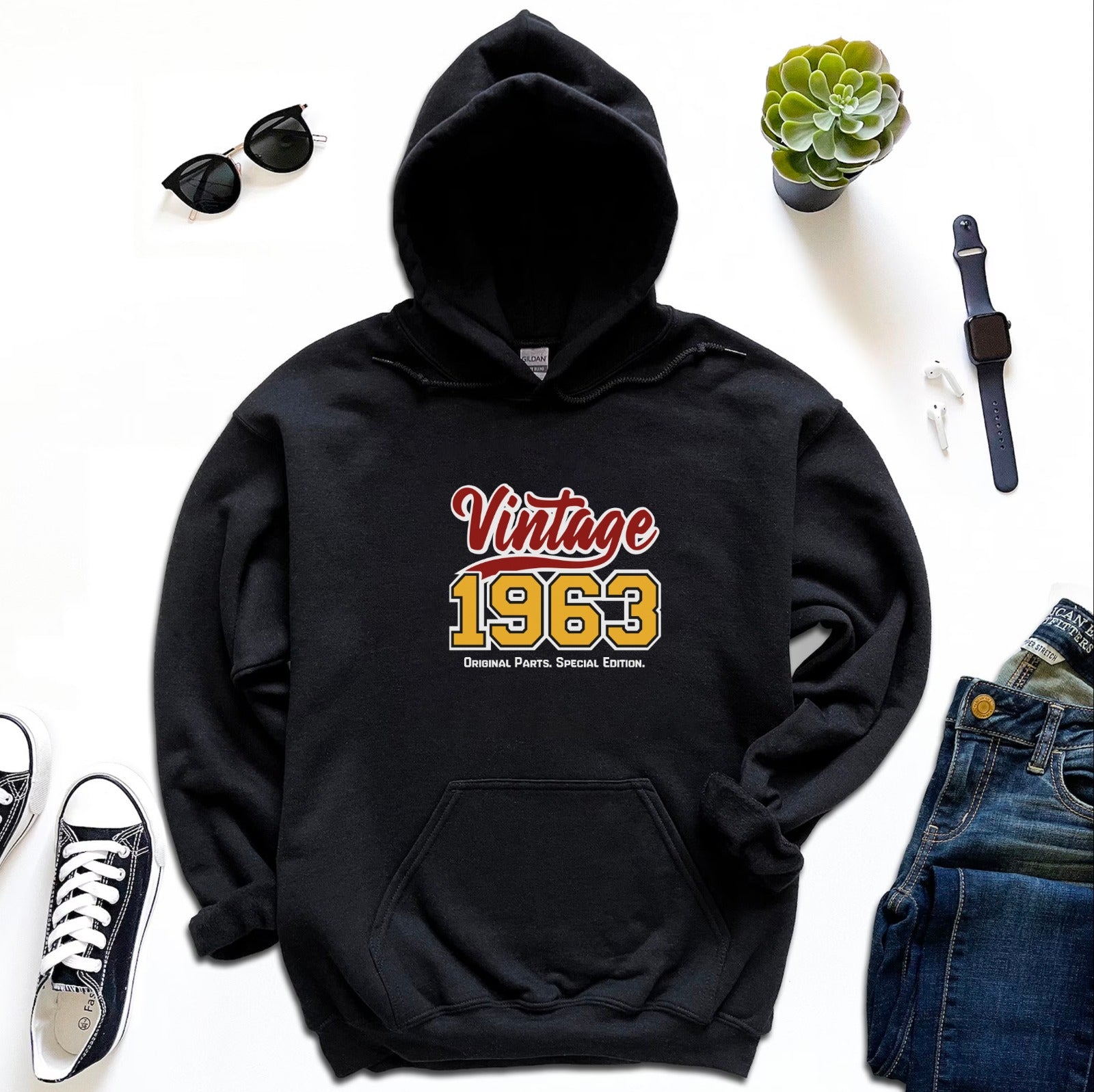 A red hoodie laid out flat with the text 'Vintage 1963' printed on the front, surrounded by accessories and clothing items.