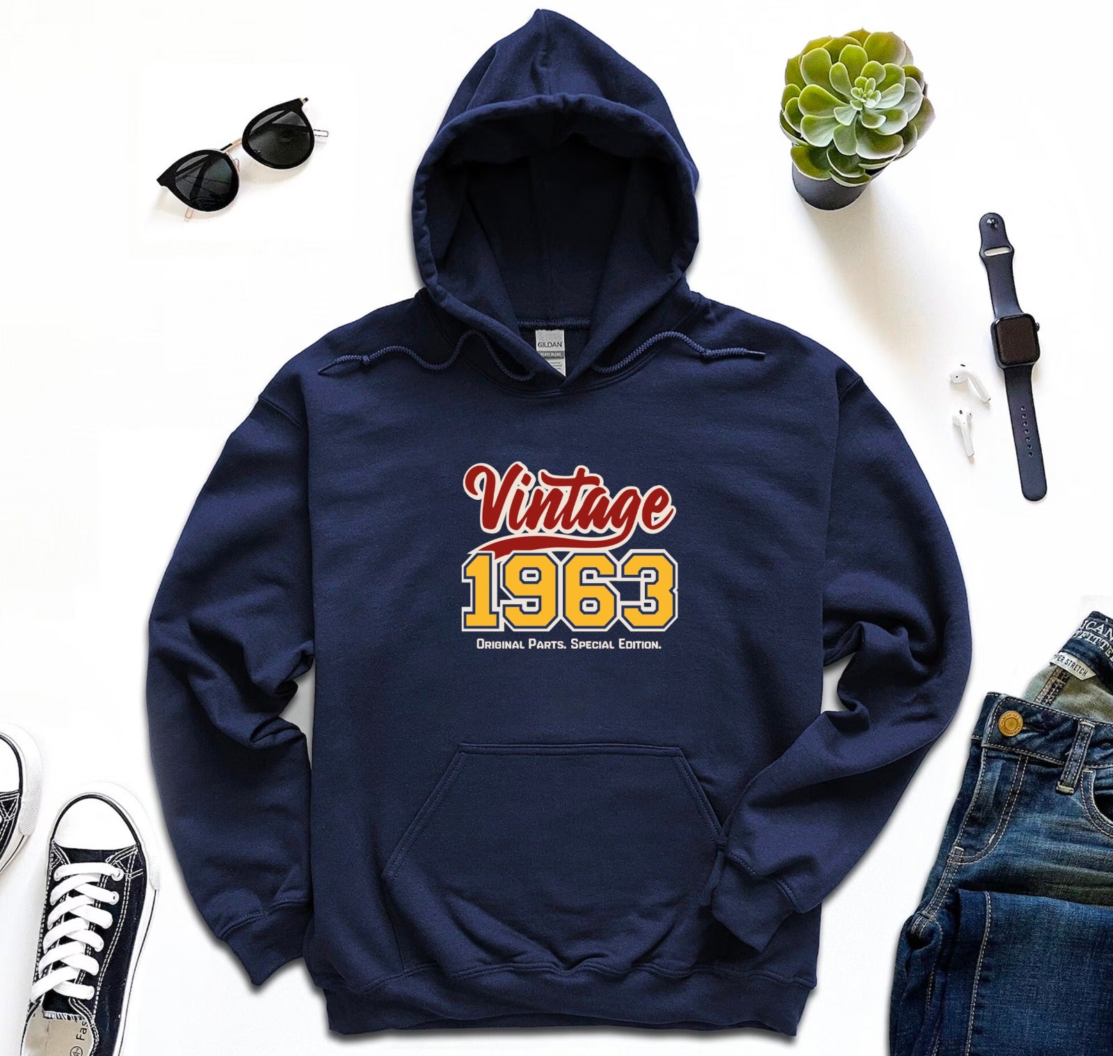 A red hoodie laid out flat with the text 'Vintage 1963' printed on the front, surrounded by accessories and clothing items.