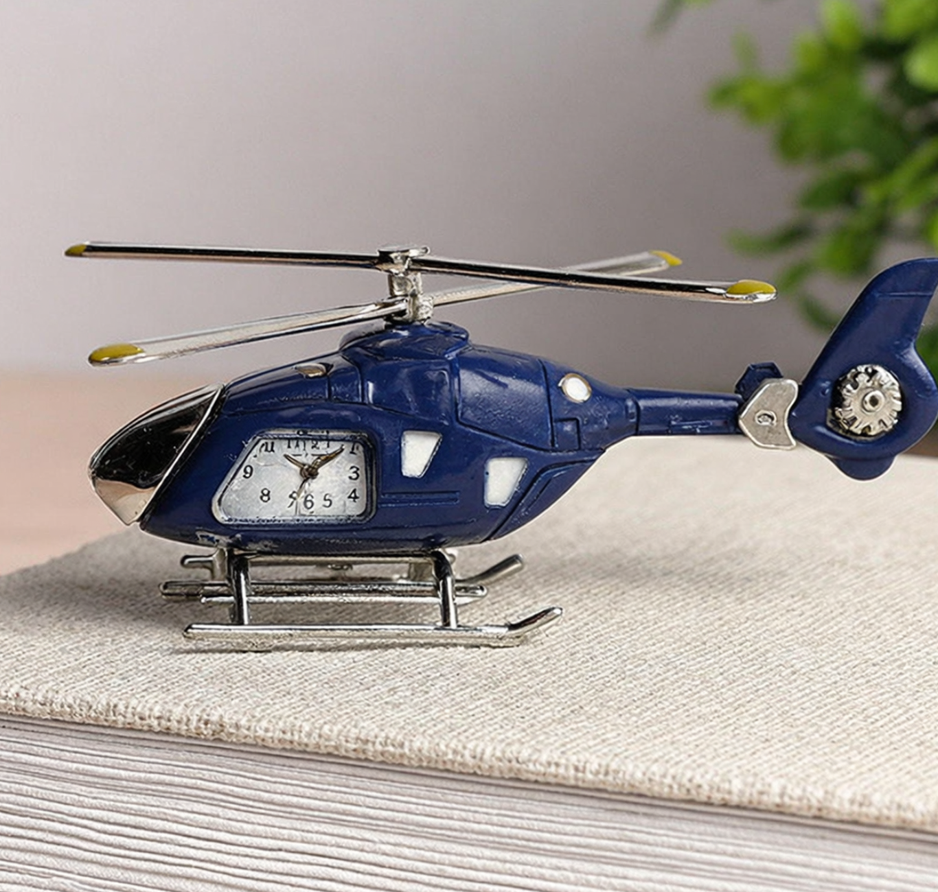 Blue helicopter-shaped clock on a textured surface with a plant in the background