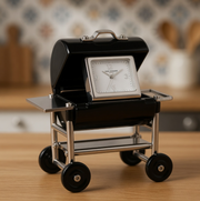 Black grill-shaped clock on wheels with a silver face, set against a blurred kitchen background.