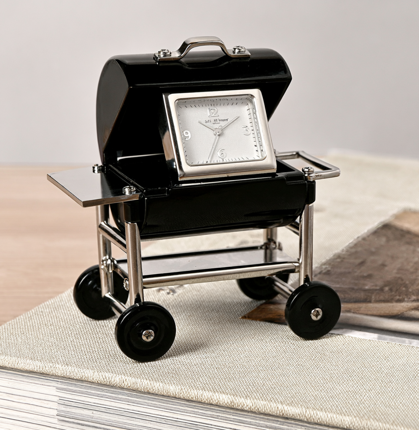 Black suitcase-shaped clock with wheels on a light surface
