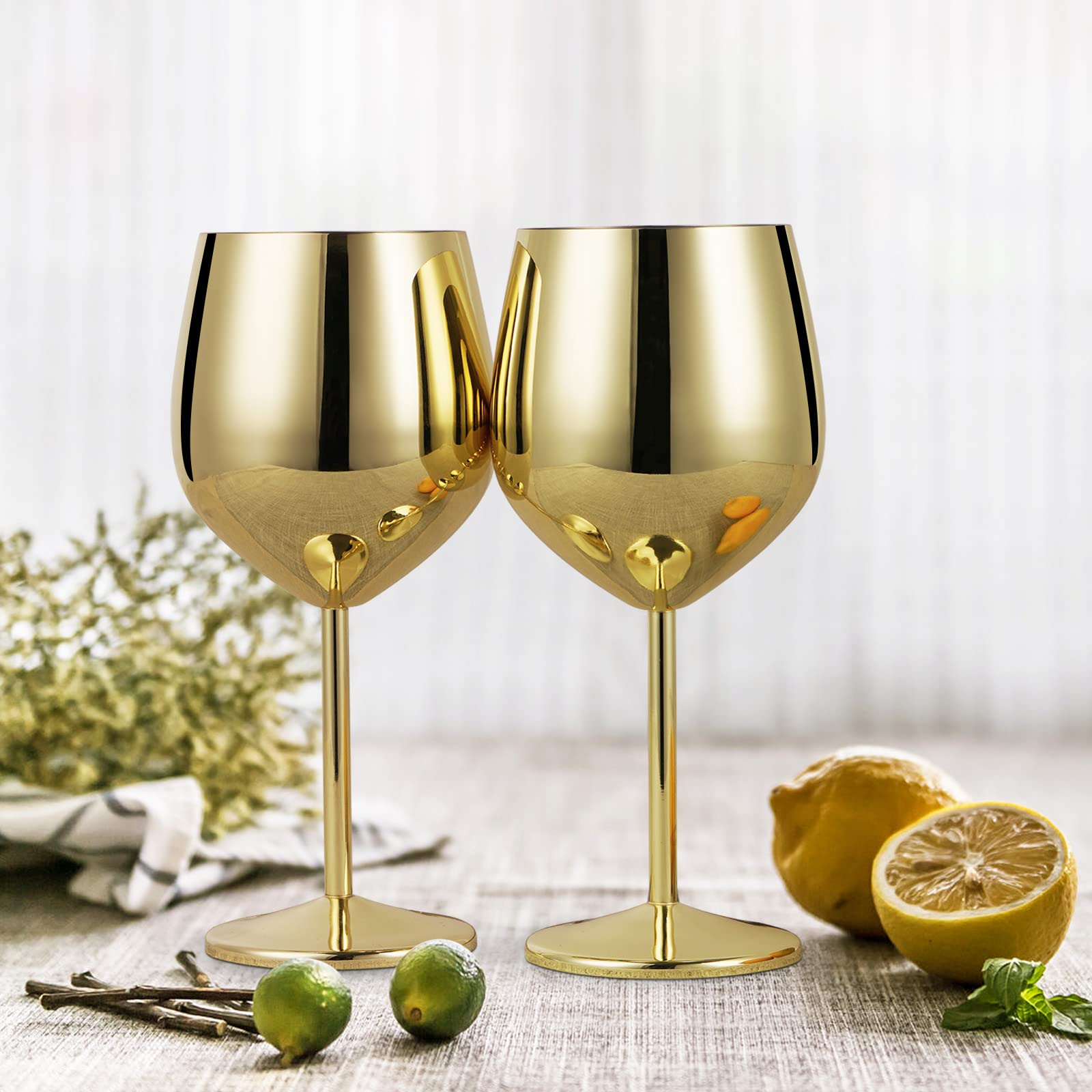 Two gold wine glasses on a table with lemons and greenery.
