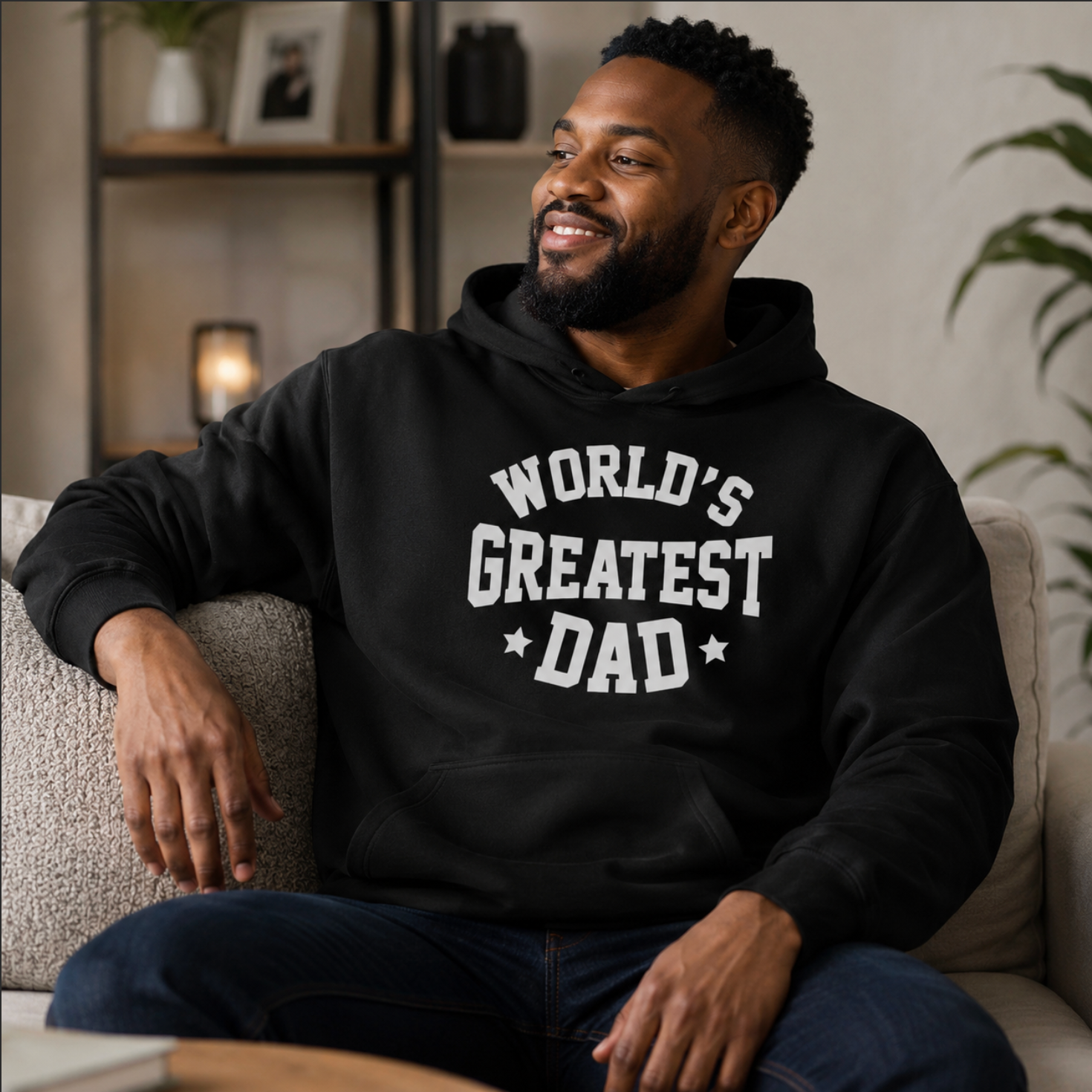 Man wearing a black hoodie with 'World's Greatest Dad' text, sitting on a couch.