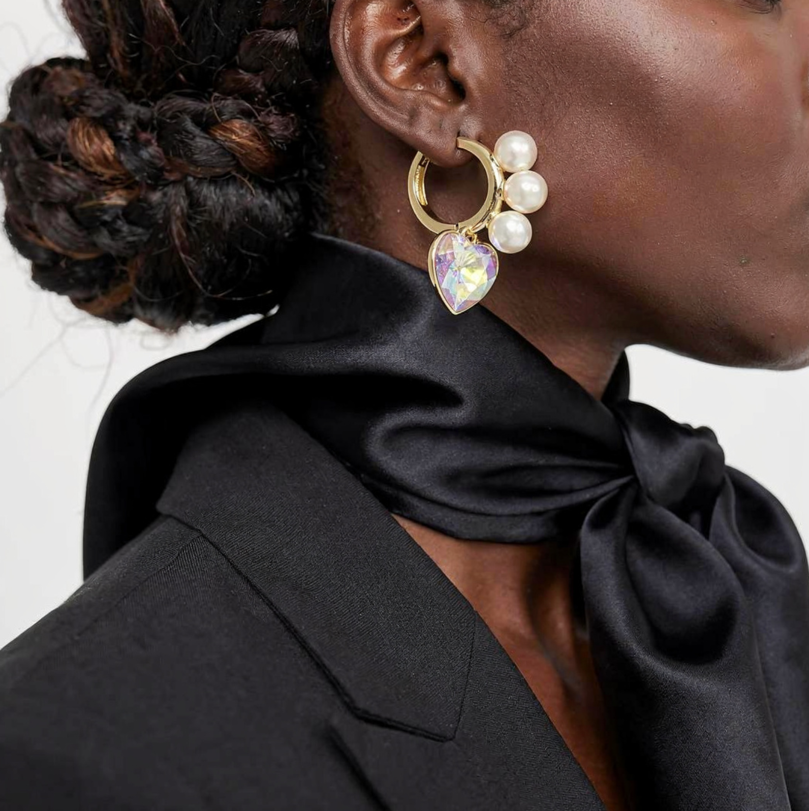 Close-up of a person wearing a gold earring with pearls and a teardrop-shaped gemstone.