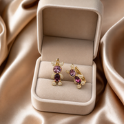 Gold earrings with purple gemstones in a beige jewelry box on a beige fabric background
