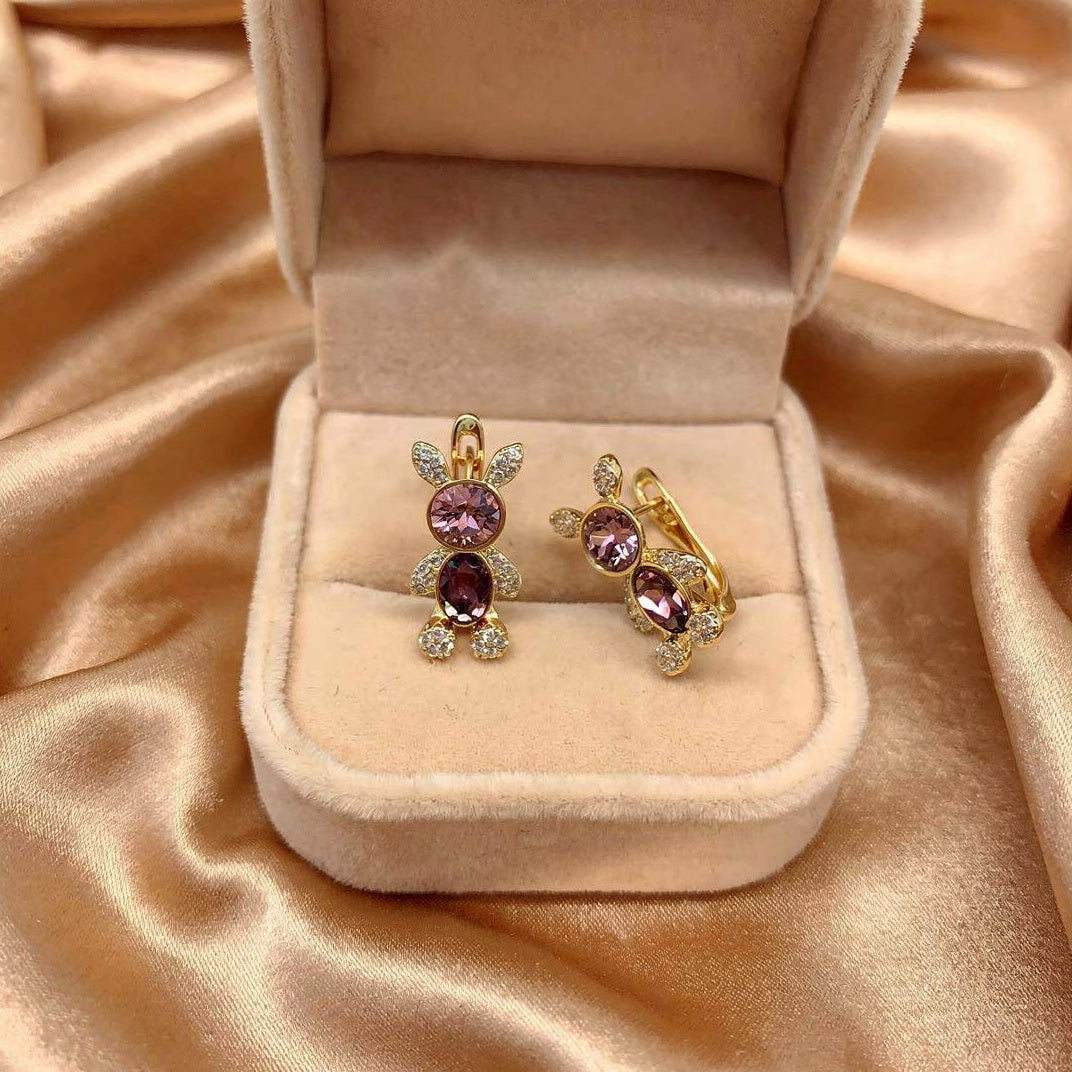 Gold earrings with purple gemstones in a beige jewelry box on a beige fabric background