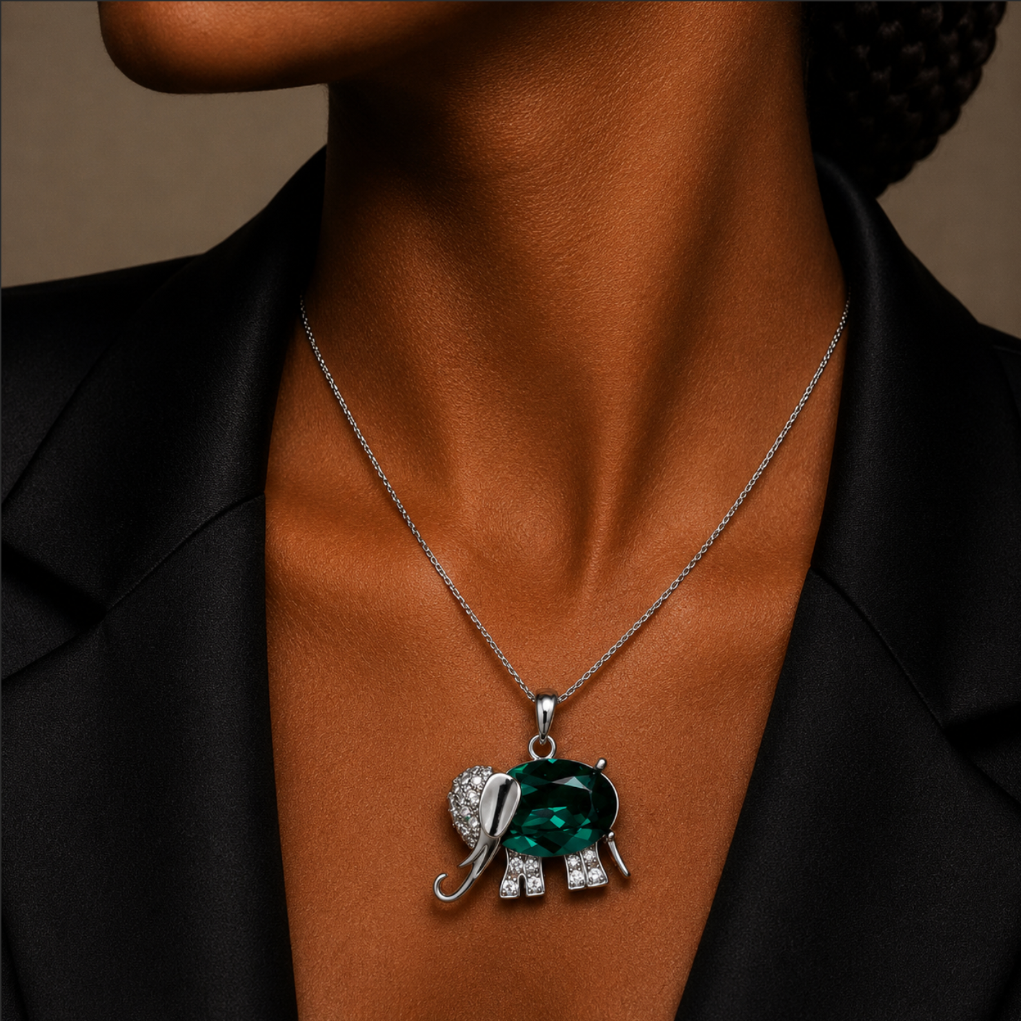 Necklace with an elephant pendant featuring a green gemstone and clear stones on a person wearing a black blazer.
