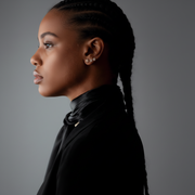 Person wearing a black satin scarf and diamond earrings against a dark background