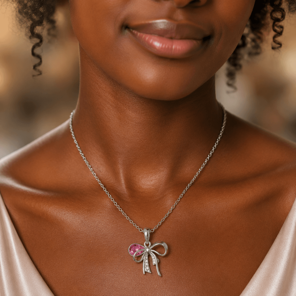 Woman wearing a silver necklace with a pink bow pendant
