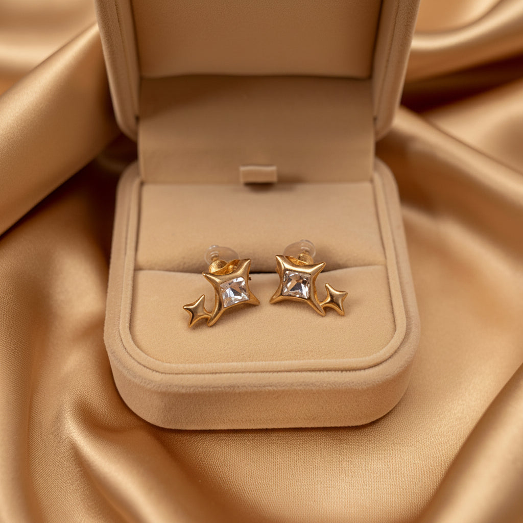 Gold earrings with star and moon design in a beige jewelry box on a satin surface