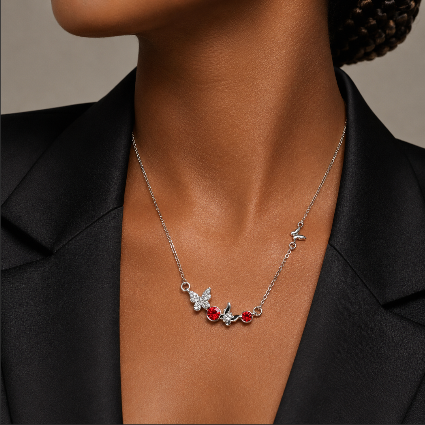 Necklace with butterfly and red gemstone pendants on a person wearing a black blazer.