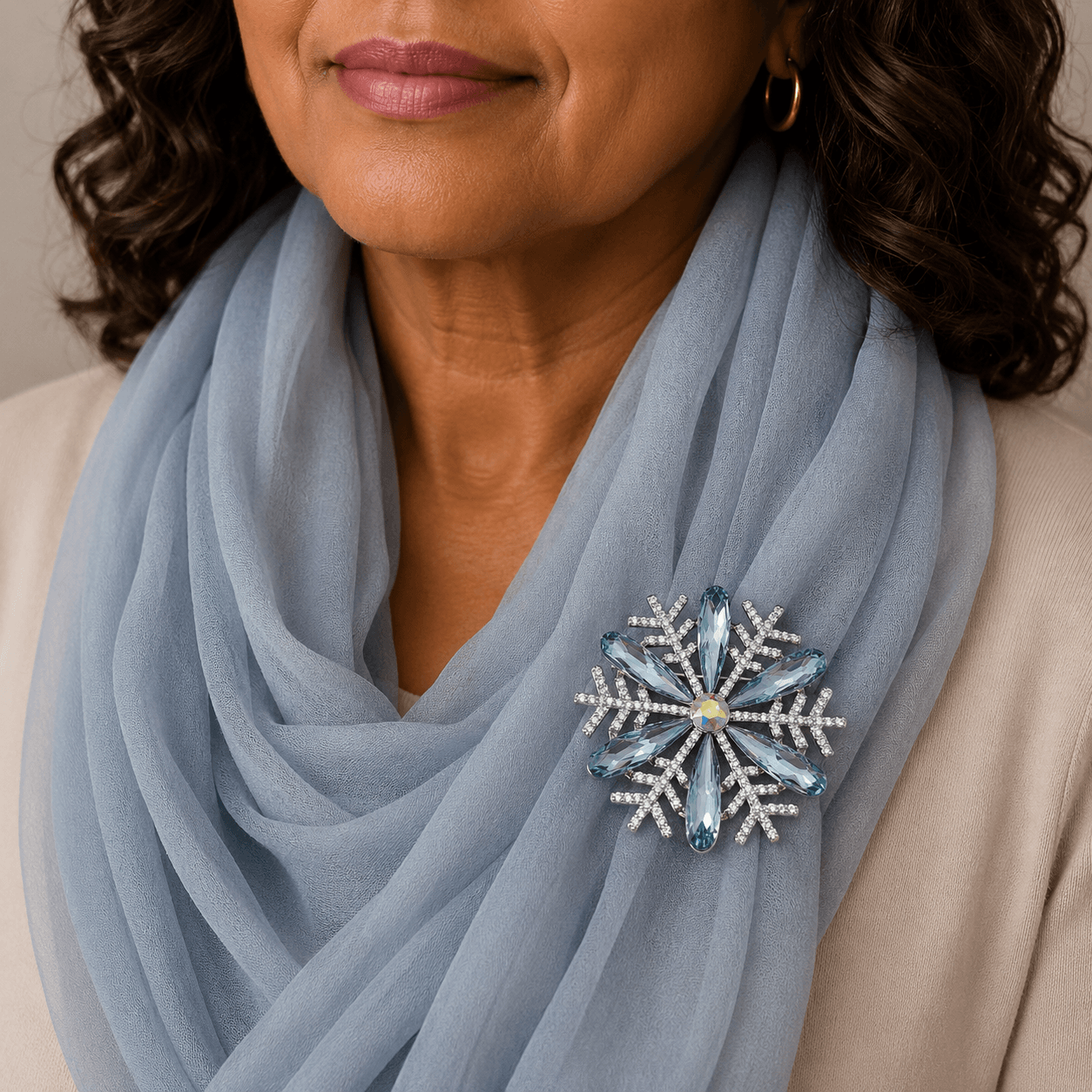 Woman wearing a light blue scarf with a decorative brooch, against a neutral background