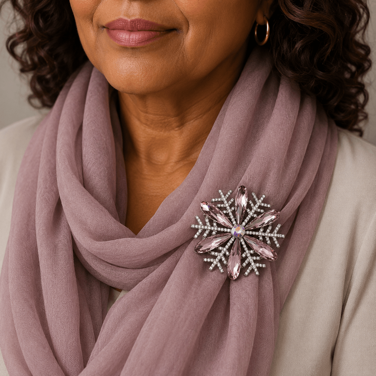 Woman wearing a mauve scarf with a decorative brooch, against a neutral background
