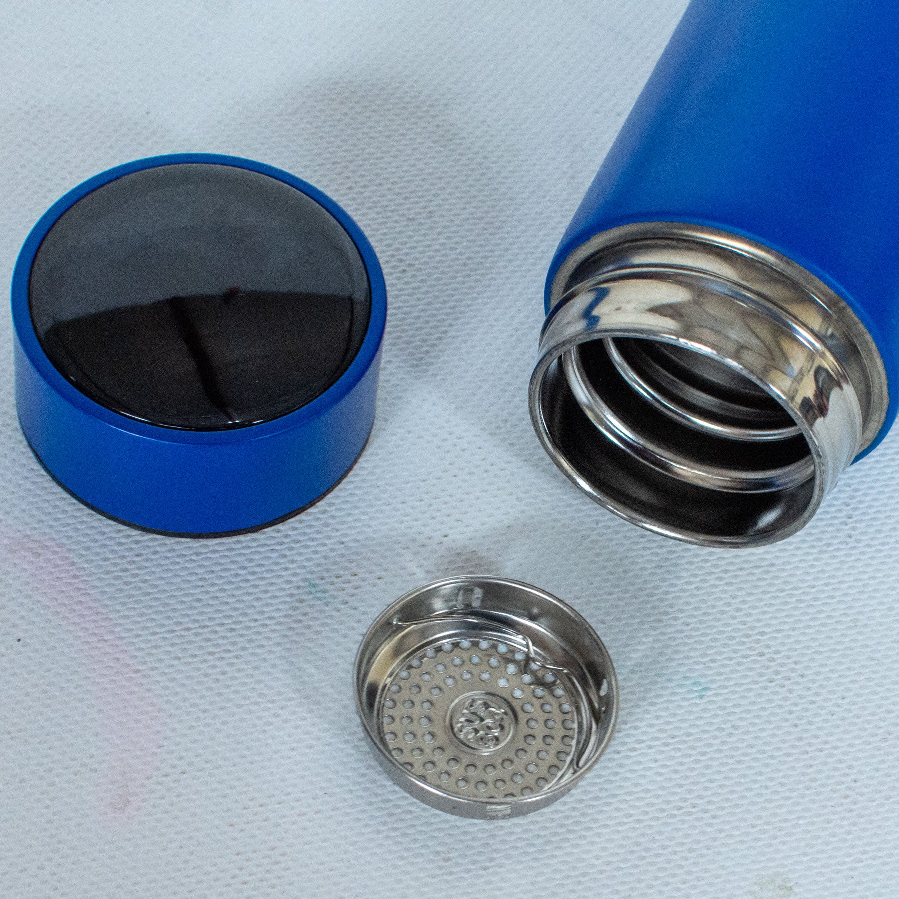 Blue thermos with black interior, silver interior lining, and metal cap on a light gray background