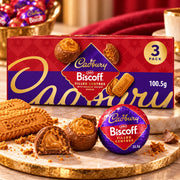 A Cadbury Biscuff filled centres 3-pack box of spread, shown with several wrapped and unwrapped chocolates and biscuit pieces on a marble board in a styled setting.