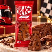 A red KitKat Official Chocolate Bar package stands on a marble surface with chocolate渣 scattered around it. A red Formula 1 helmet and checkered flag appear blurred in the background, and several KitKat chocolate bars and broken pieces are placed in front of the package.