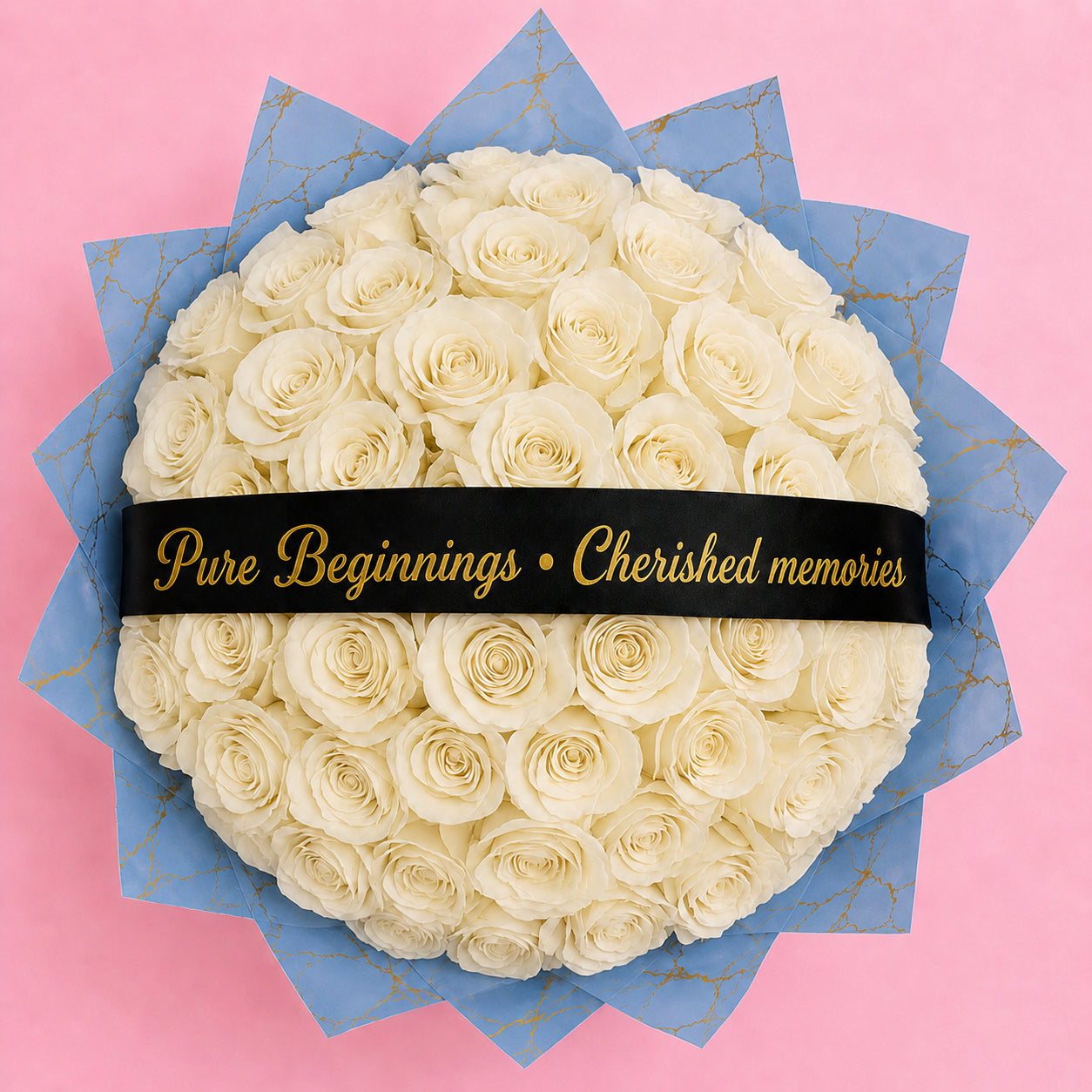 A round bouquet of white roses wrapped in blue paper with gold veins and a black ribbon across the middle that reads 'Pure Beginnings • Cherished memories' in gold lettering, set against a solid pink background.